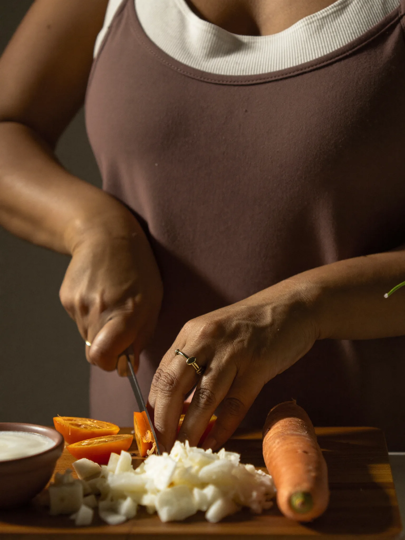 Hands slicing fresh vegetables on a wooden board in warm light