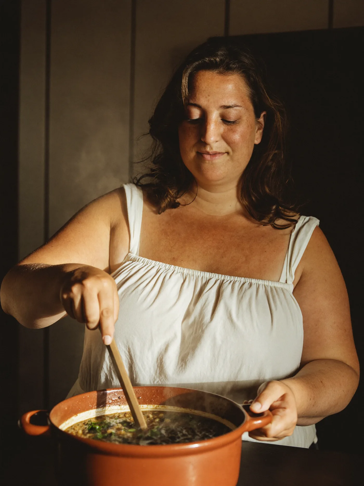 Woman cooking a warming lentil and spinach stew in a terracotta pot