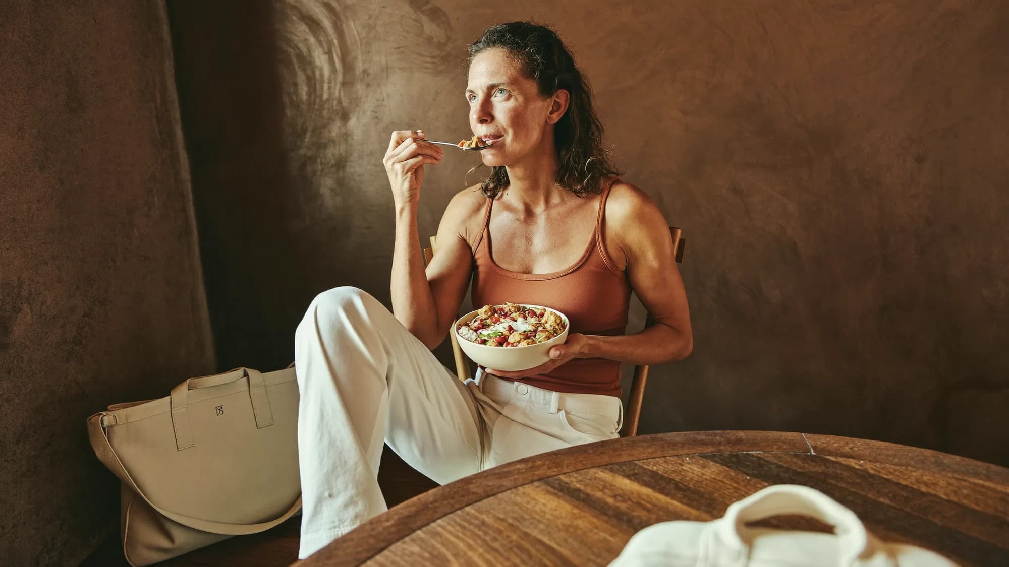 Athletic woman eating a protein-rich bowl at a wooden table after training